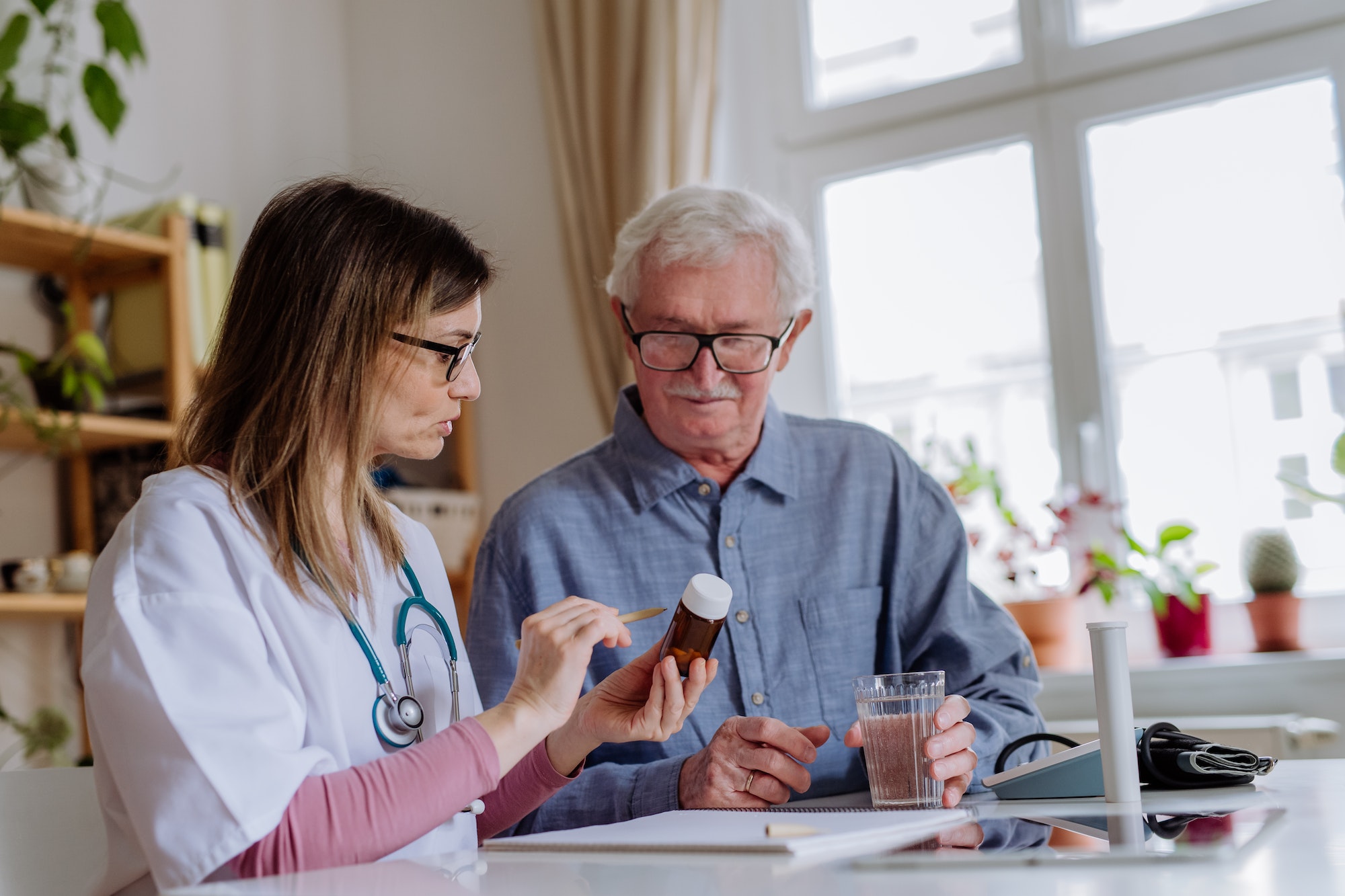 Healthcare worker or caregiver visiting senior man indoors at home, explaining medicine dosage.